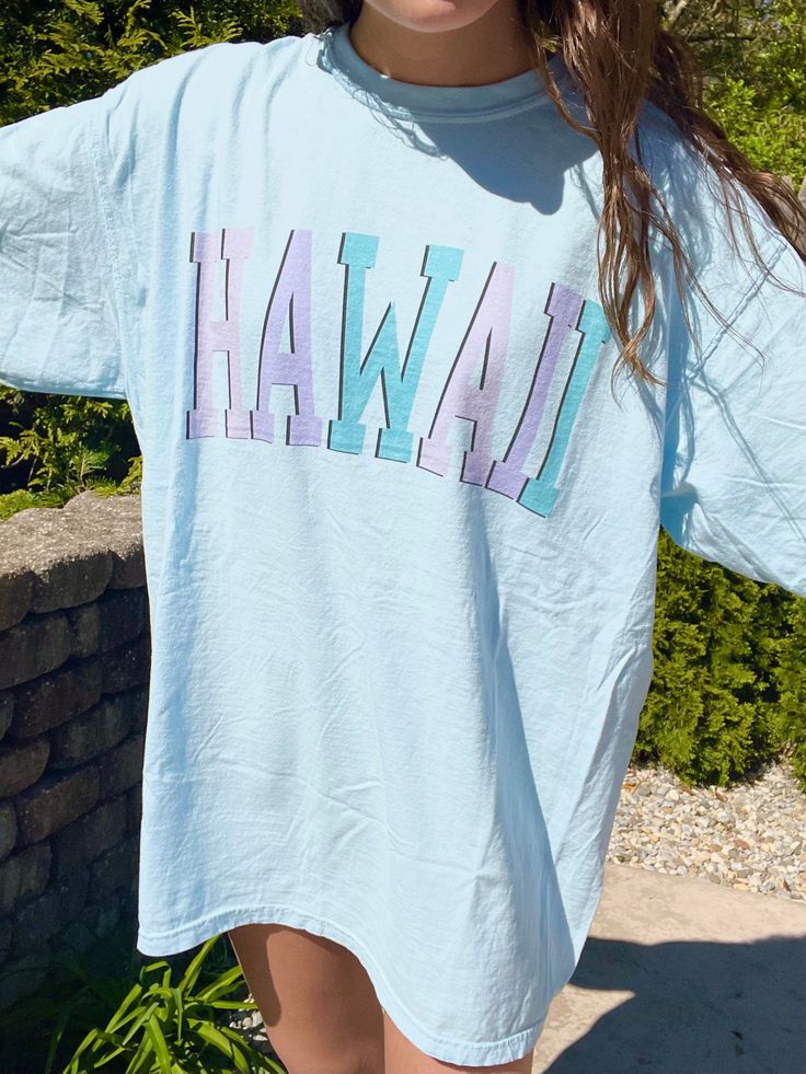 "Such a cute tee for summer! Comfort Colors chambray (light blue) t-shirt with \"HAWAII\" in blue and purple, with a black outline. Model is 5'4\" and wearing a size XL for an oversized look. 100% cotton." Trendy Light Blue Spring T-shirt, Casual Light Blue T-shirt For Summer, Light Blue Short Sleeve T-shirt For Summer, Light Blue T-shirt With Letter Print For Spring, Trendy Light Blue Graphic Print T-shirt, Blue Cotton T-shirt For Summer, Summer Blue T-shirt For Streetwear, Blue Text Print Top For Summer, Blue Tops With Text Print For Summer