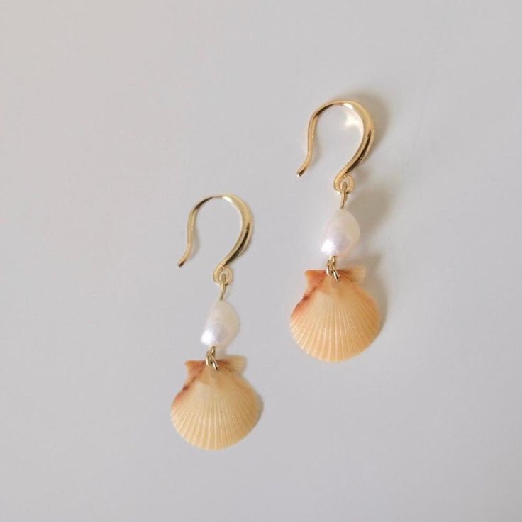 a pair of seashells with pearls hanging from them on gold ear wires against a white background