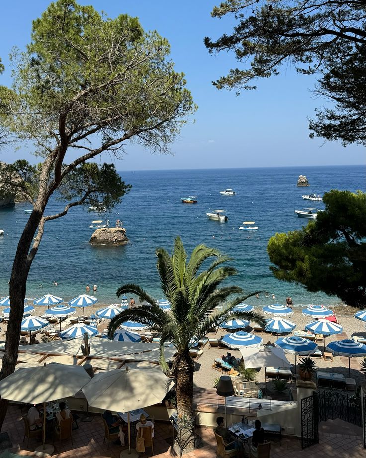 the beach is crowded with umbrellas and boats in the water near trees, sand and rocks