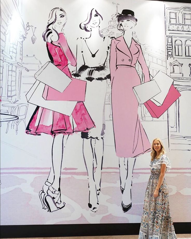 a woman standing in front of a drawing of two women wearing dresses and hats on the wall