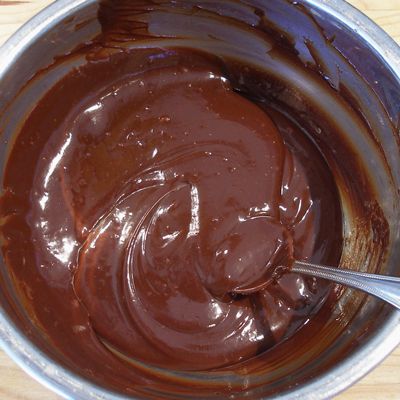 a metal bowl filled with melted chocolate on top of a wooden table next to a spoon