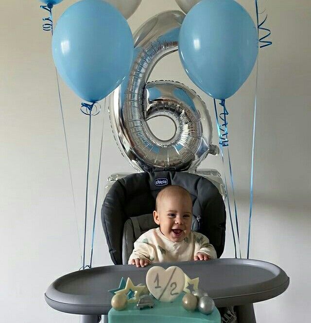 a baby sitting in a high chair with balloons around him and a cake on the table