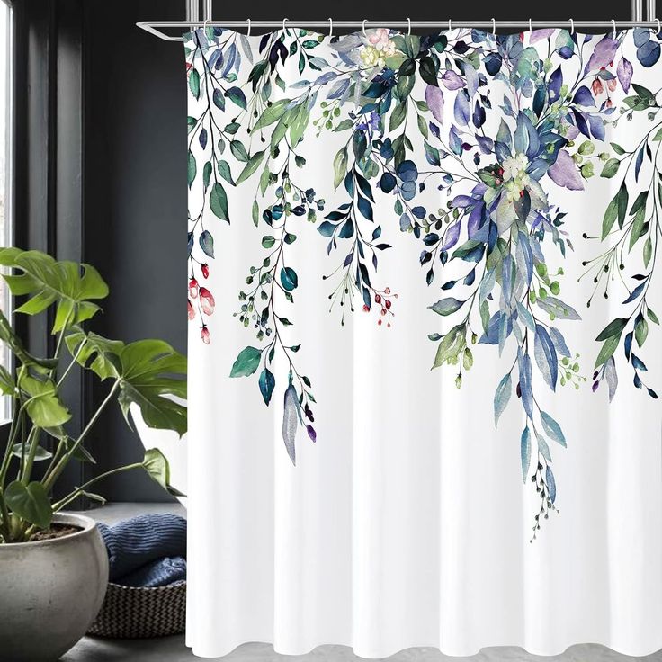 a white shower curtain with blue and green leaves on it next to a potted plant