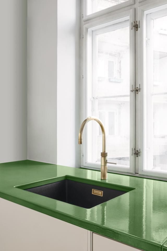 a green counter top next to a window in a room with white walls and windows