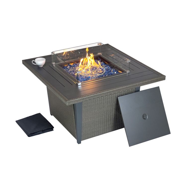 an outdoor fire pit sitting next to a table with a cup on it and a laptop