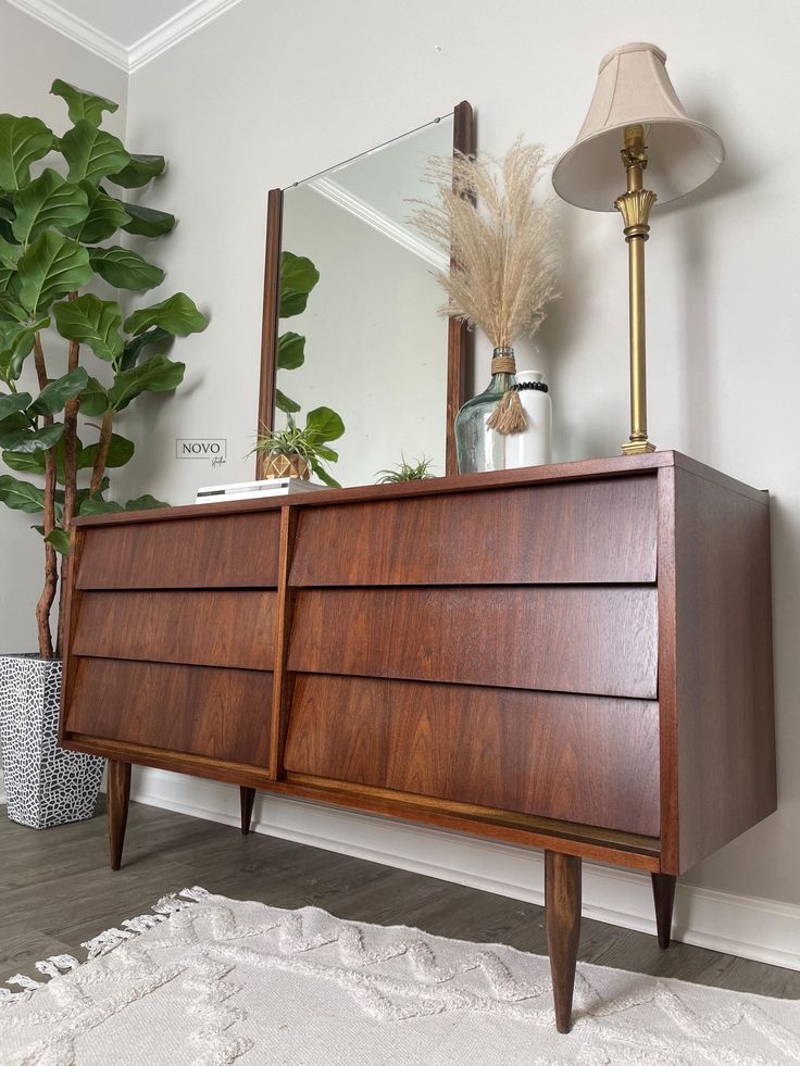 a large wooden dresser sitting next to a mirror and potted plant in a living room