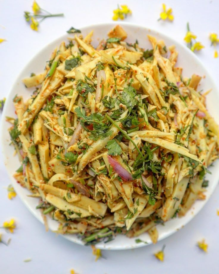 a white plate topped with pasta covered in greens and seasoning next to yellow flowers