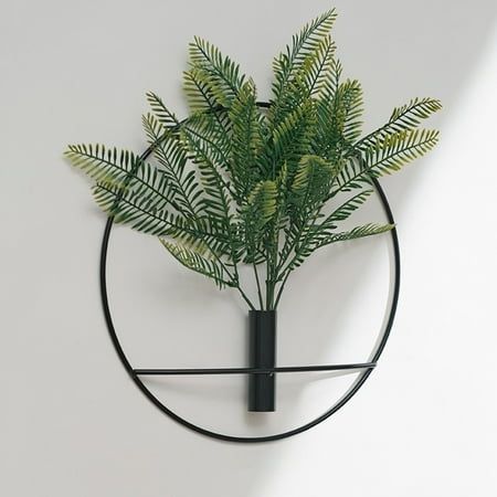 a green plant is placed in a circular metal holder on the wall above a white wall