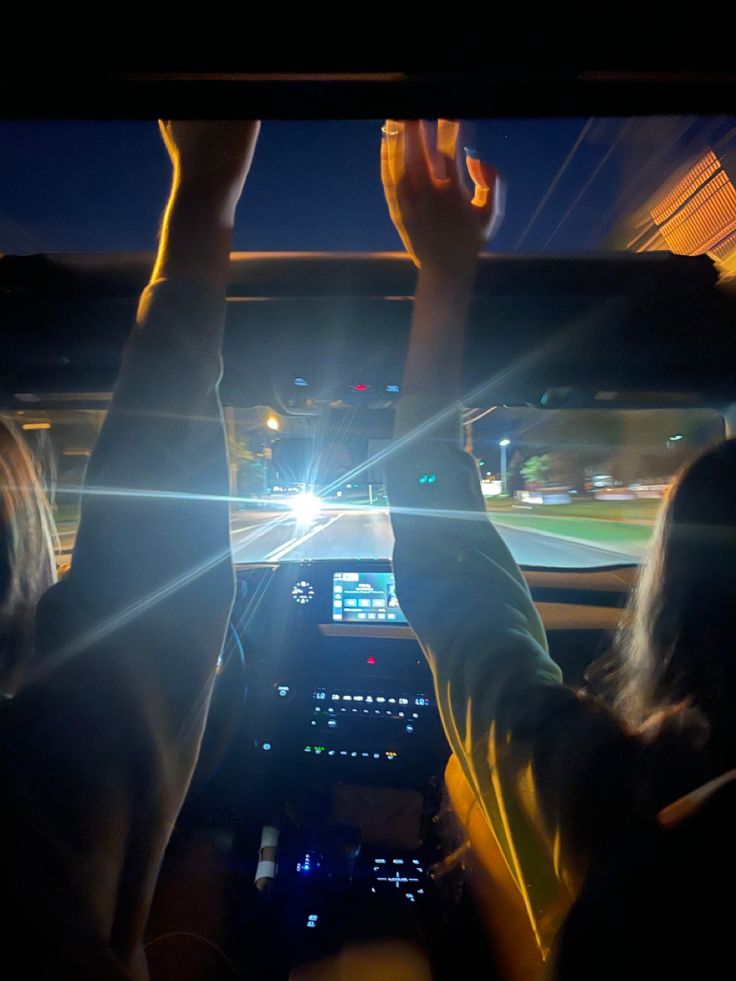 two people in the back seat of a car with their hands up and lights on