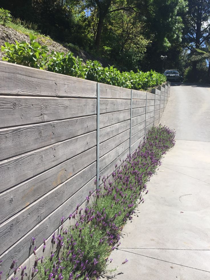 purple flowers are growing on the side of a wooden fence in front of a road