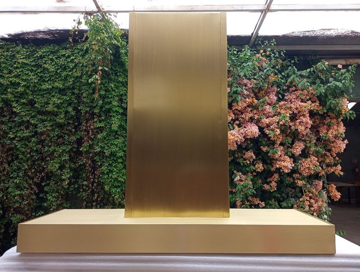 a gold sculpture sitting on top of a table in front of a wall covered with flowers