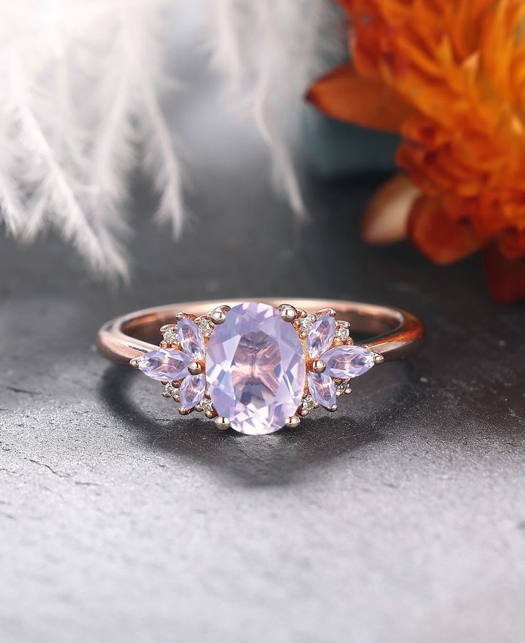 an image of a ring with three stones on it and flowers in the back ground