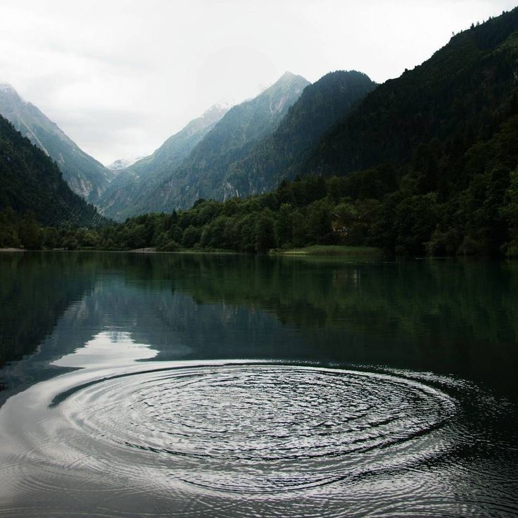 a body of water surrounded by mountains and trees in the distance with a circular design on it