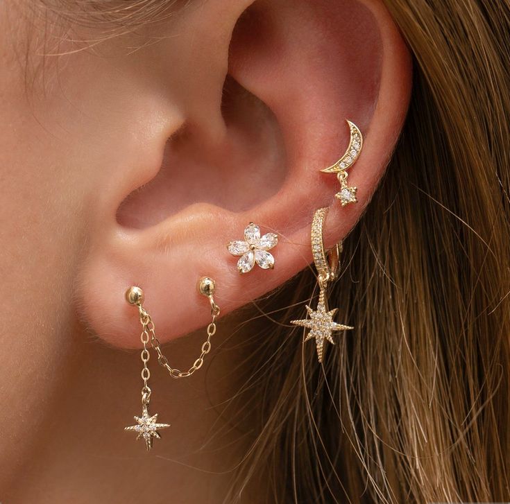 a woman's ear is adorned with three stars and a crescent, which are dangling from the back of her ear