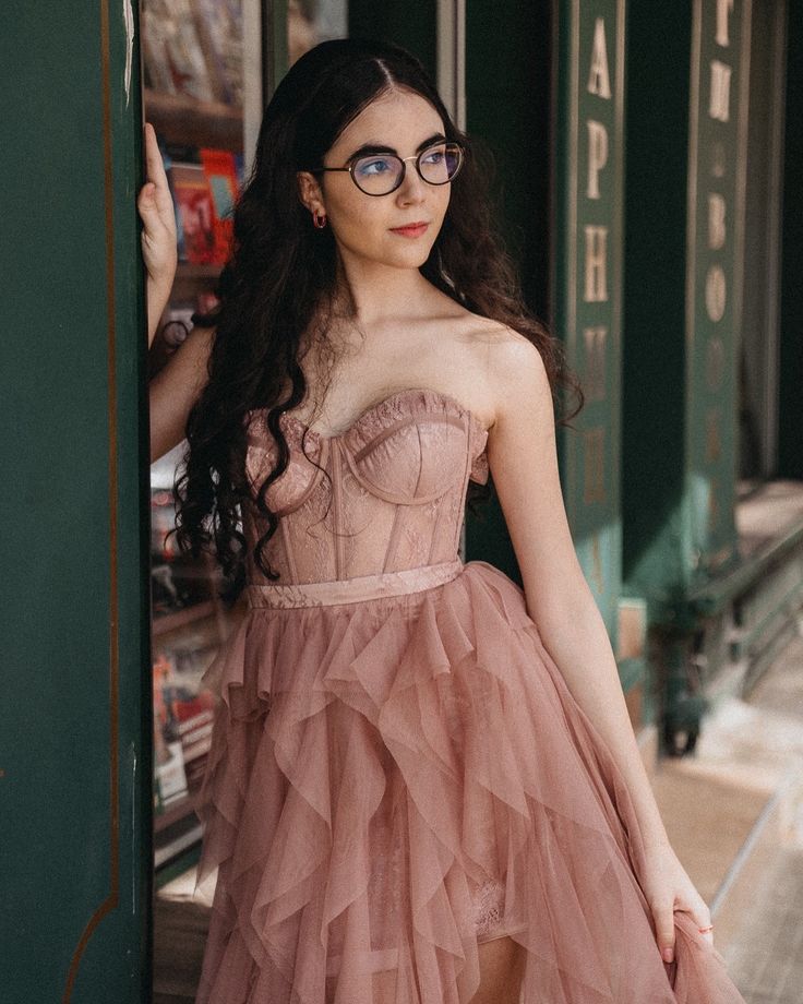 a woman in a pink dress leaning against a wall with her hands on her hips