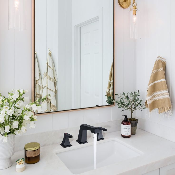 a bathroom sink with a mirror above it and flowers in the vase on the counter