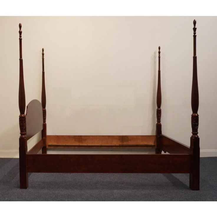 a wooden bed frame with two posts and a mirror on the bottom one side, in front of a white wall