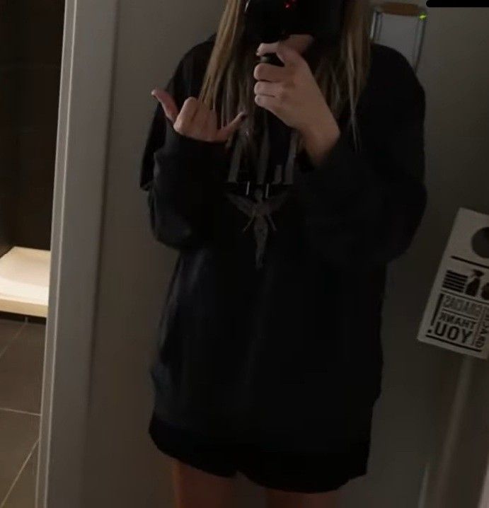 a woman standing in front of a mirror holding a cell phone up to her face