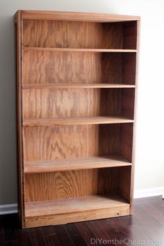 an empty wooden bookcase sitting on top of a hard wood floor next to a wall