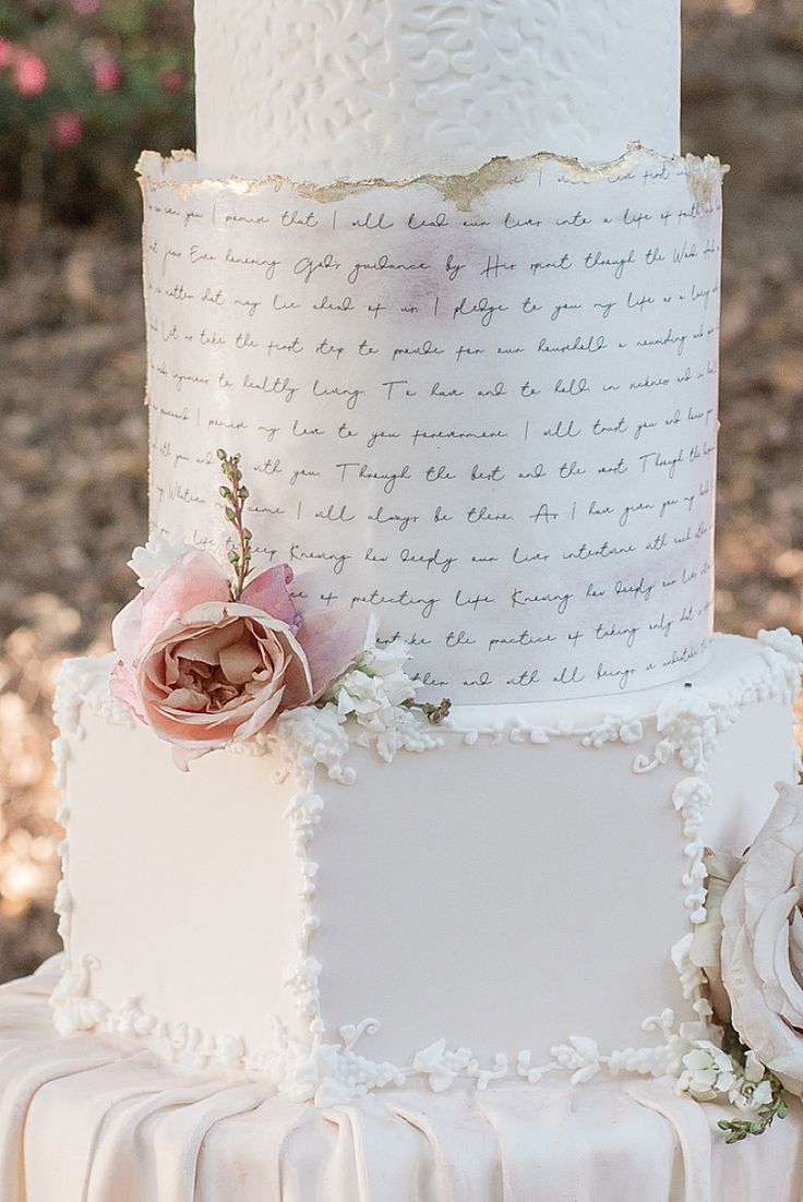 a three tiered wedding cake with flowers on top and writing on the bottom layer