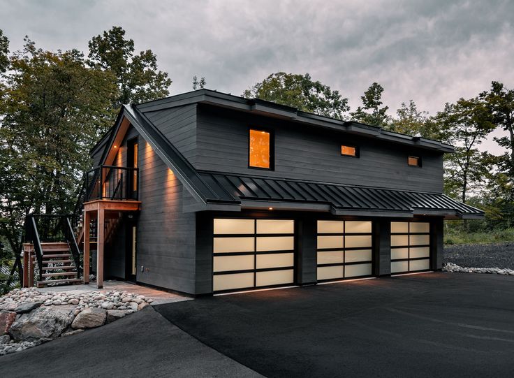 a black house with two car garages on the front and second story is lit up at night