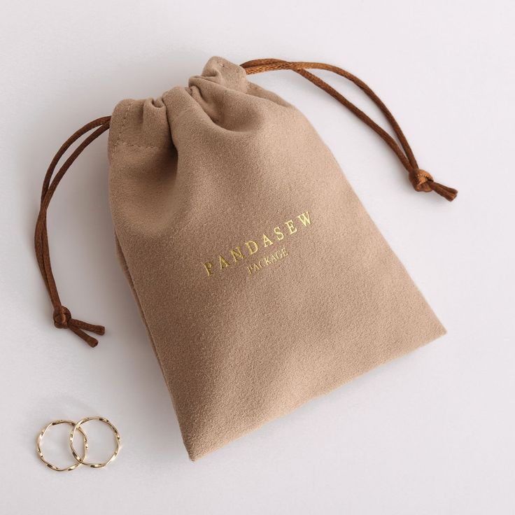 a small bag with two gold rings on the side and a pair of earrings next to it