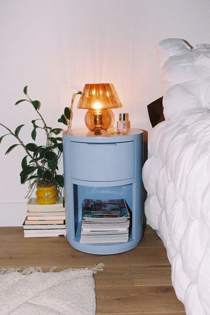 a nightstand with a lamp on top of it next to a bed and a plant