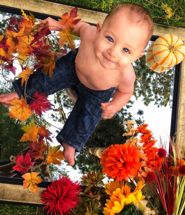 a baby is sitting in front of a mirror with fall leaves and flowers around it