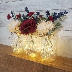 three glass vases with flowers and lights in them