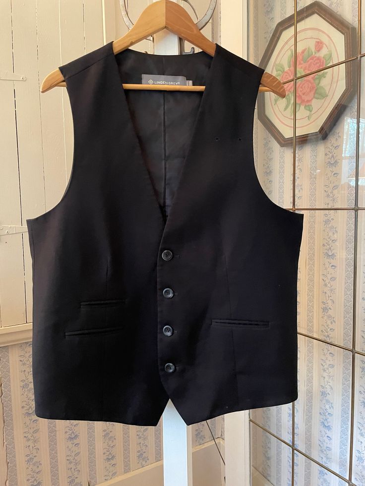 This beautiful vest was made by Linden Grey in a very soft blend of 54 per cent polyester, 44 per cent cotton and 2 per cent Lycra in classic black. It has the original buttons and three pockets in the front that haven't been used (they haven't been unsewn) and two tiny openings on the front left for a name tag to fit through. Marked size 44 regular. The measurements, taken with the vest lying flat, are: shoulder to shoulder, 15 inches; armpit to armpit, 23 inches; length, 28 inches in front and 24 1/2 inches in back; bottom edge, 23 inches. In very good condition. Wool Vest With Pockets For Work, Sleeveless Business Vest Outerwear, Black Sleeveless Vest With Pockets, Business Vest With Pockets, Sleeveless Business Vest With Pockets, Formal Winter Sleeveless Vest, Formal Sleeveless Winter Vest, Tailored Black Vest Outerwear, Classic Black Vest For Business