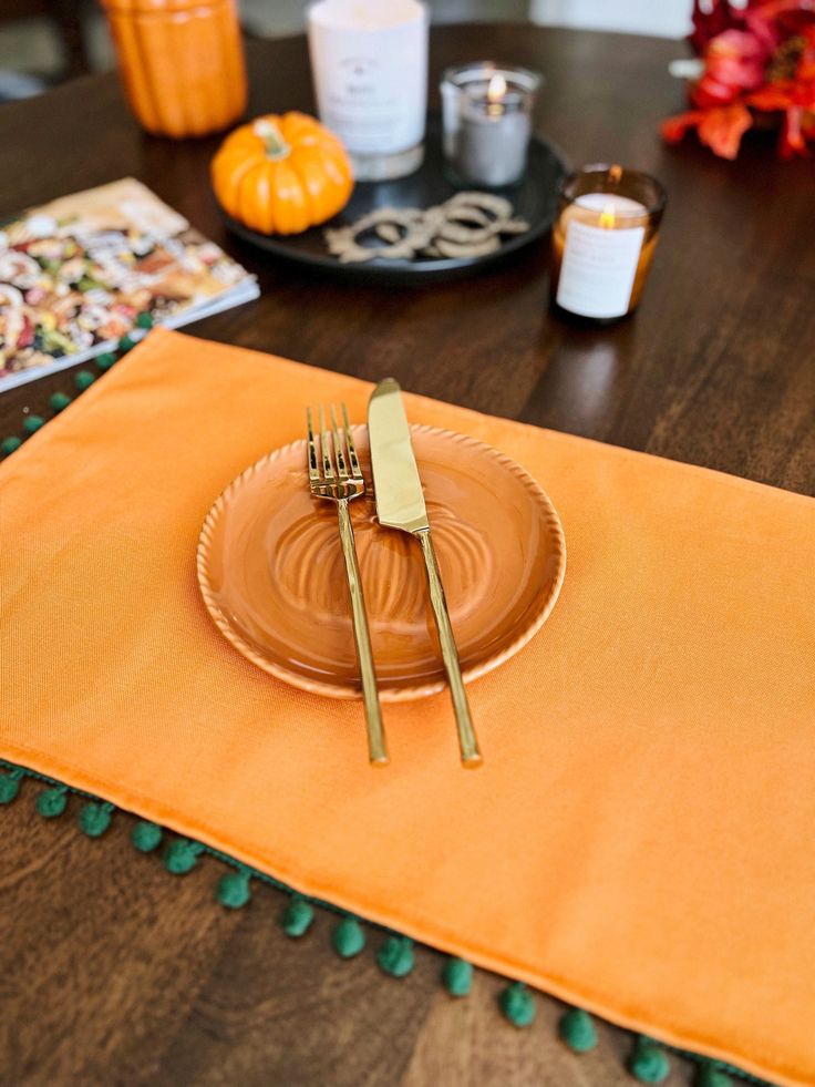 a place setting with orange napkins and gold forks