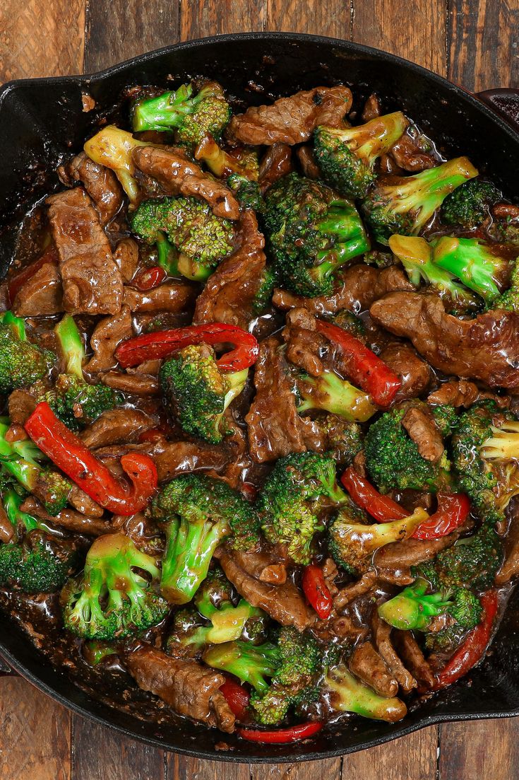 beef and broccoli stir fry in a skillet on top of a wooden table