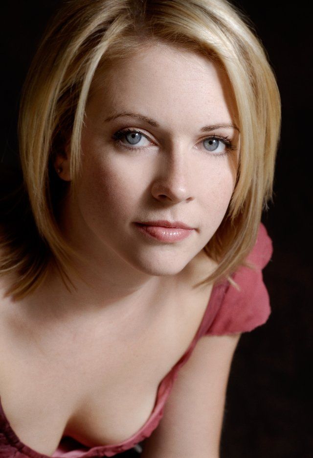 a woman with blonde hair and blue eyes is posing for a photo in front of a black background