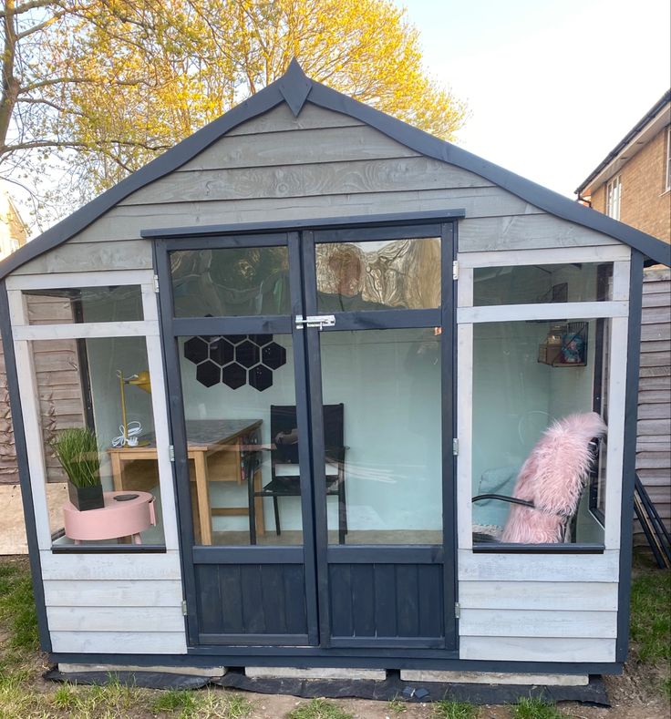 a small shed with two windows and a pink feather on the outside, sitting in front of a house