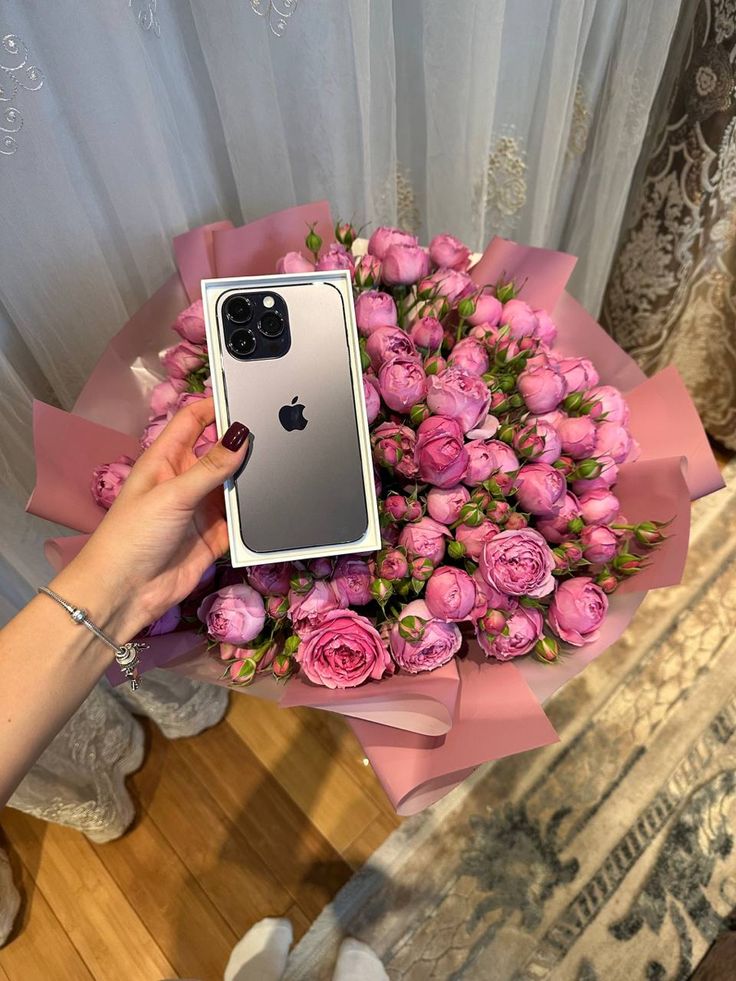 a bouquet of pink roses is being held by a woman with an iphone in her hand