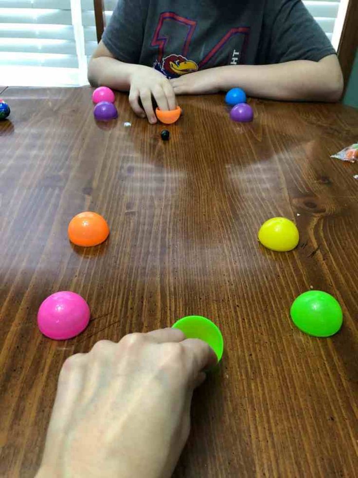 a child is playing with plastic balls on a wooden table in front of an adult