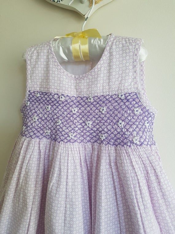 This gorgeous dress is made with 100% cotton lilac and white printed fabric which is fully lined with a soft white fabric. The dress is elegantly hand smocked and adorned with hand embroidered detail, back closes with buttons and a tie back waist.  Size 3 - Length of Dress from back of neckline to Spring Cotton Dress With Smocked Back, Pink Cotton Sundress With Smocked Back, Fitted Cotton Sundress With Smocked Back, Fitted Purple Dress With Smocked Bodice, Purple Fitted Dress With Smocked Bodice, Fitted Purple Dresses With Smocked Bodice, Cotton Smocked Dress For Spring, Spring Cotton Dress With Smocked Bodice, Cotton Sundress With Smocked Bodice For Garden Party