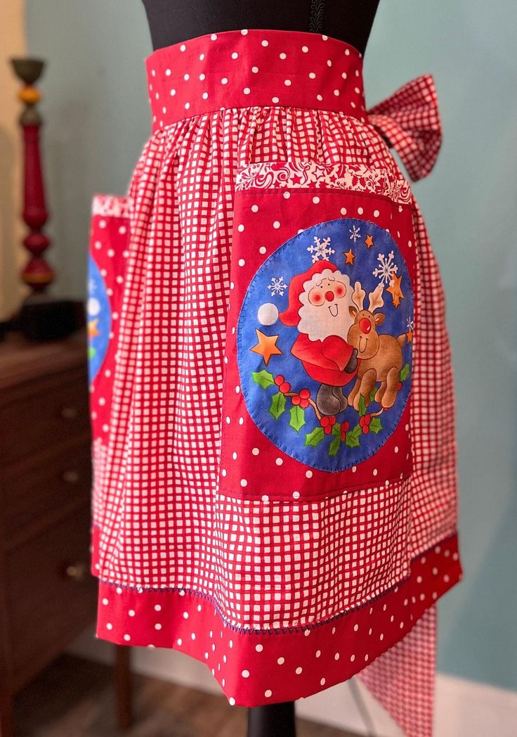 a red and white apron with santa clause on it's chest, attached to a mannequin