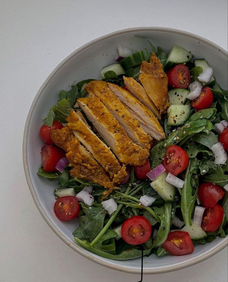 a white bowl filled with salad and sliced chicken on top of it's side