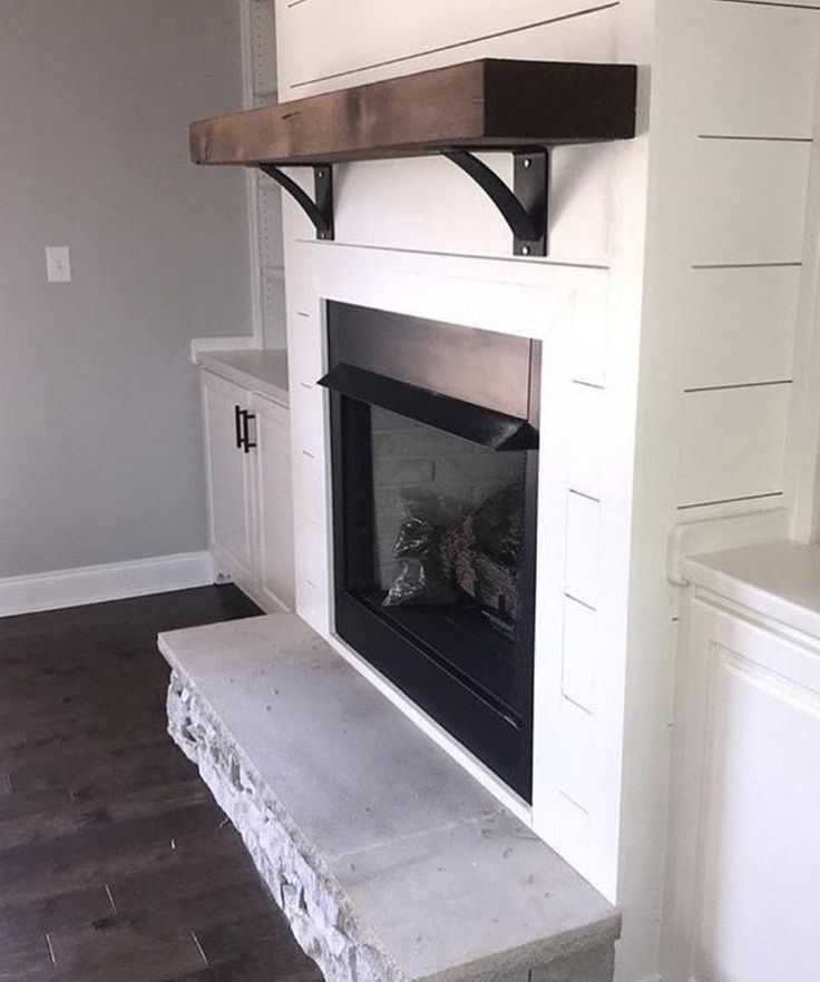 an empty fireplace in the corner of a room with white walls and wood flooring