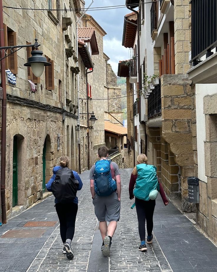 three people walking down an alley way with backpacks on their back and one person carrying a blue bag