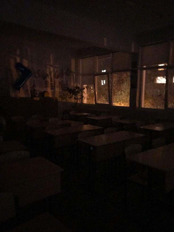 an empty classroom with desks and chairs in the dark, lit up by windows