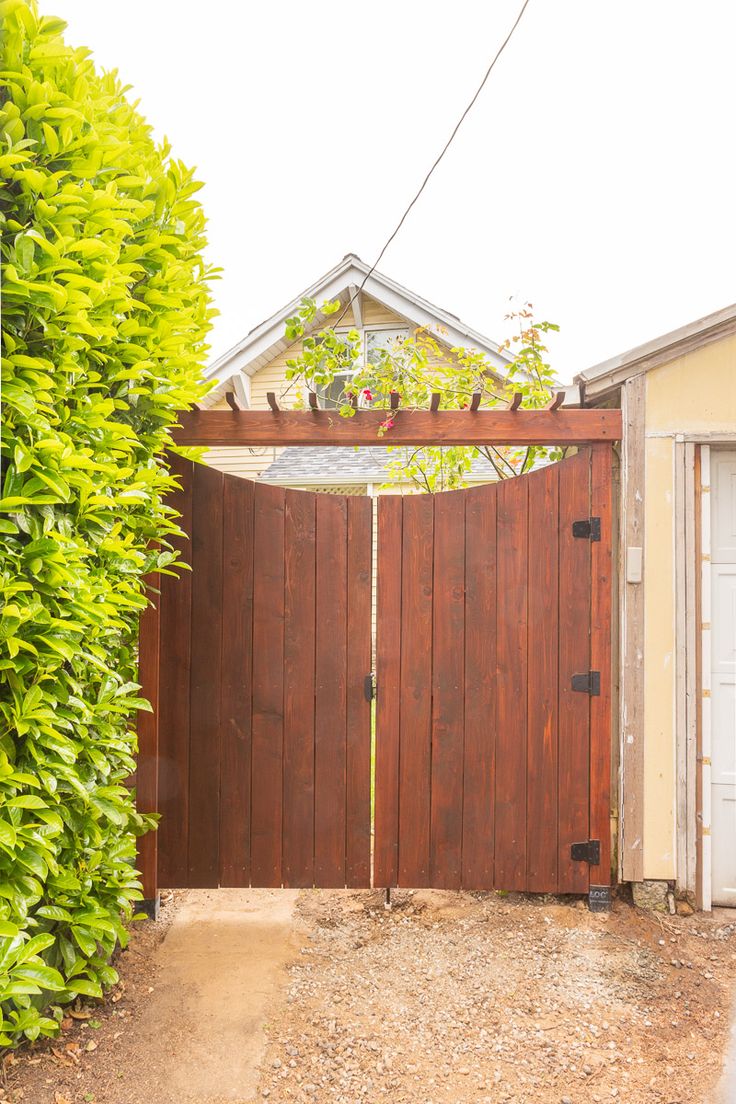 a wooden gate in front of a house with a green bush growing on the side