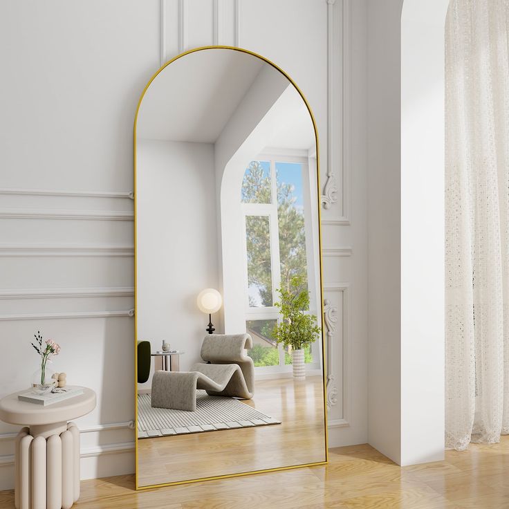 a large gold framed mirror sitting on top of a wooden floor next to a window