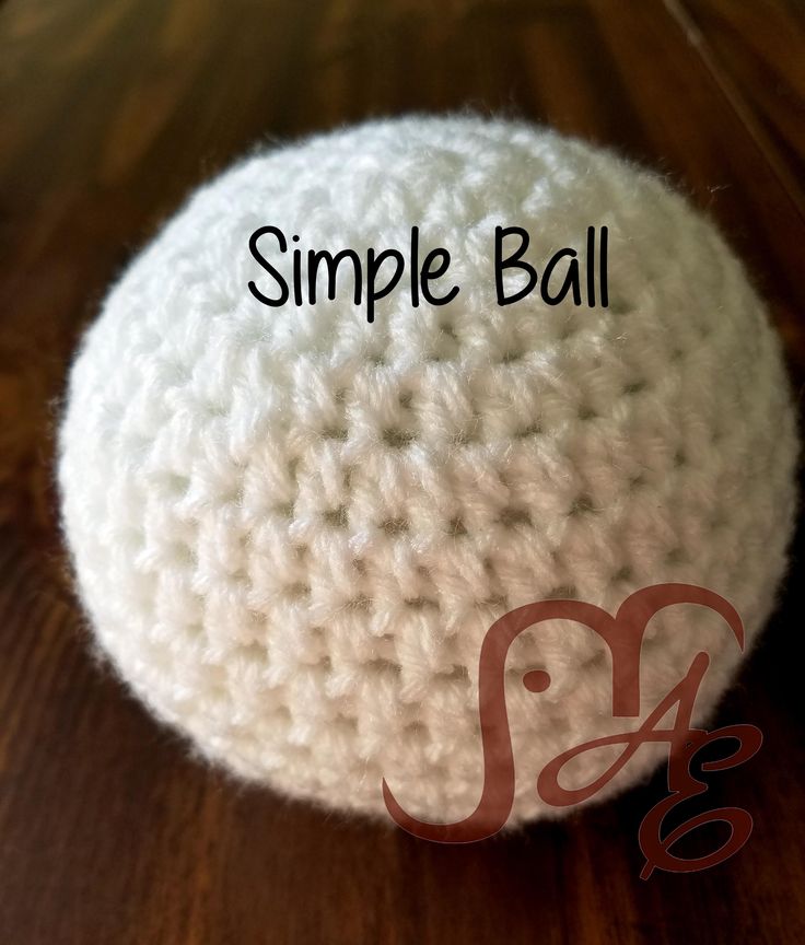 a white crocheted ball sitting on top of a wooden table with the words simple ball written across it