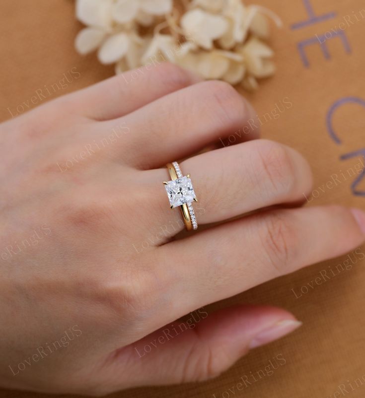 a woman's hand with a ring on her finger and flowers in the background