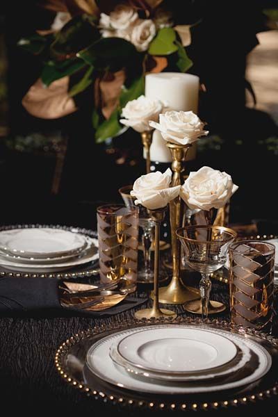 the table is set with gold and white plates, silverware, and candlesticks