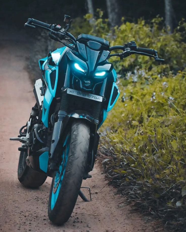 a blue motorcycle parked on the side of a dirt road next to bushes and trees