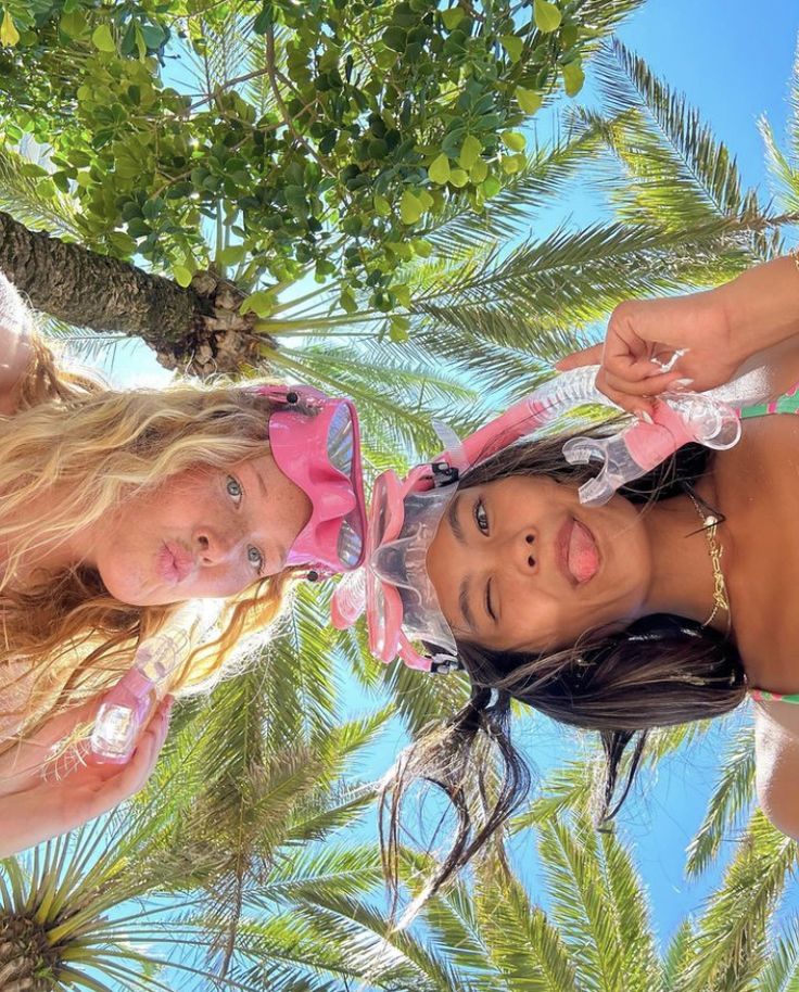 two beautiful young women standing next to each other under a palm tree on the beach