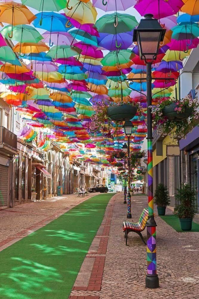 many colorful umbrellas are hanging from the ceiling above an empty street lined with shops